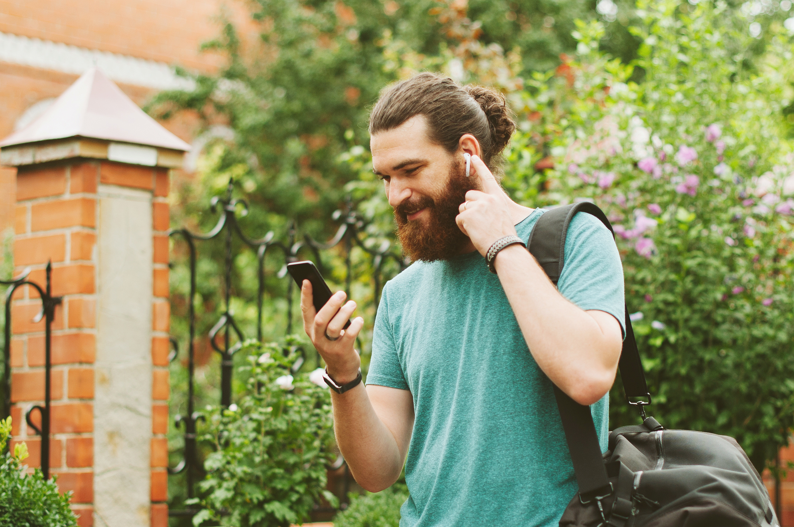 Cheerful happy bearded man looking at his smartphone, listening to the music with earpods outdoors. Cheerful happy bearded man looking at his smartphone, listening to the music with earpods outdoors.